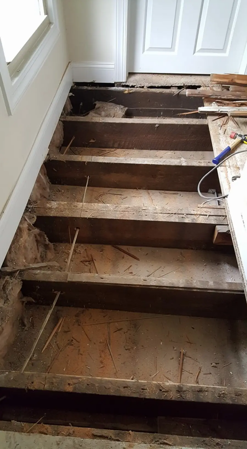 The hardwood being ripped up exposes the joists and stringers of the floor at the top of the stairs.
