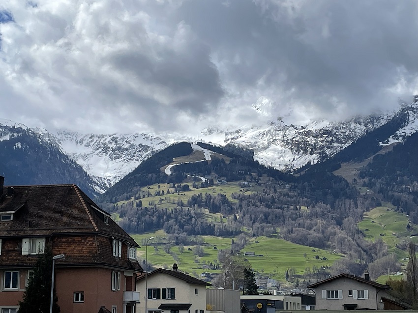 A view of a mountain with a ski slope on it, the snow melting and its turning green